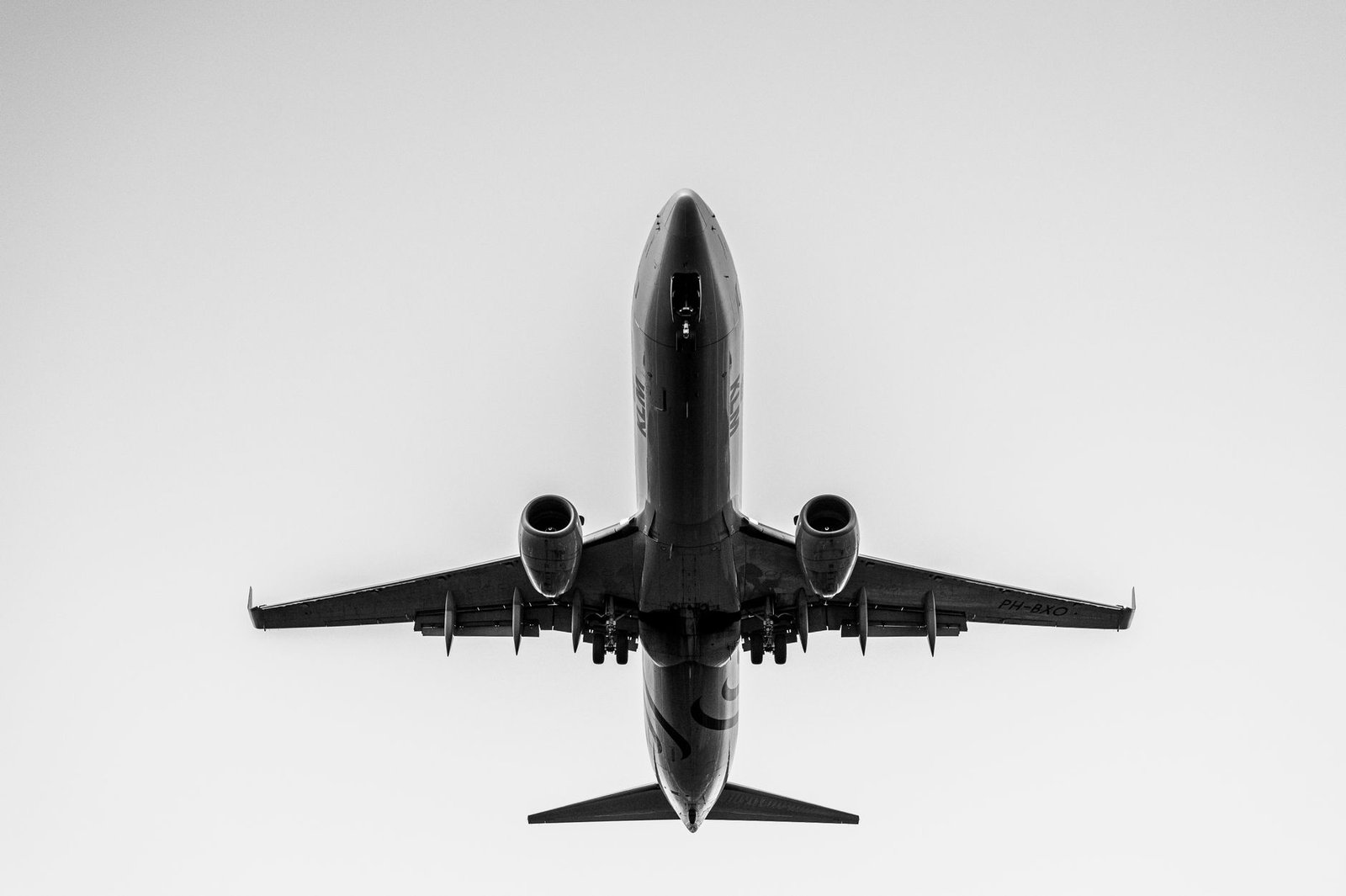 A black and white image of a passenger airplane captured from below, flying overhead.