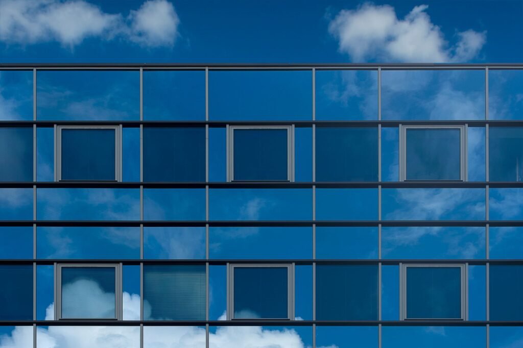 Facade of a modern glass building reflecting the blue sky and clouds.