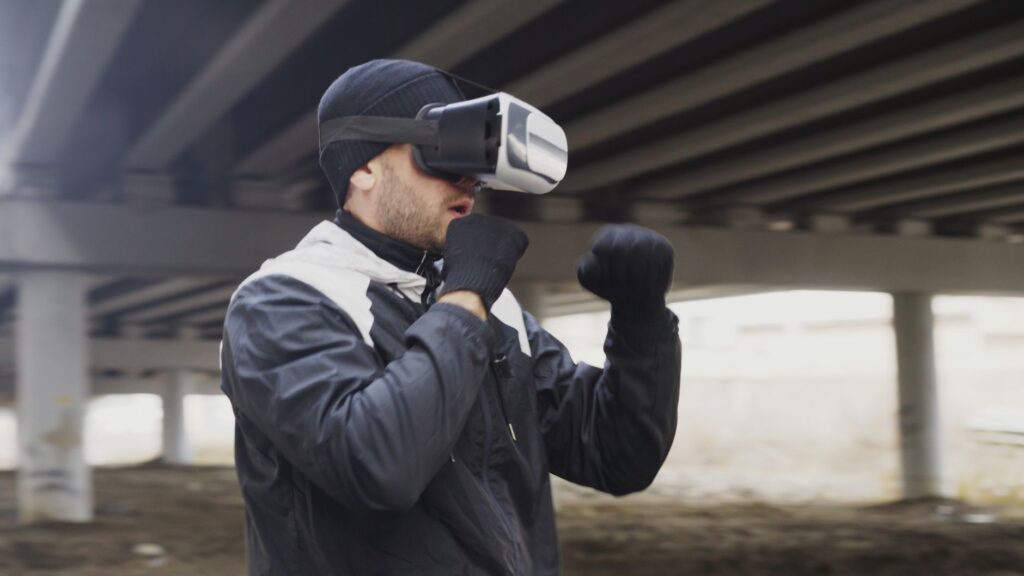 Adult male exercises with VR headset, simulating boxing outside in urban setting.