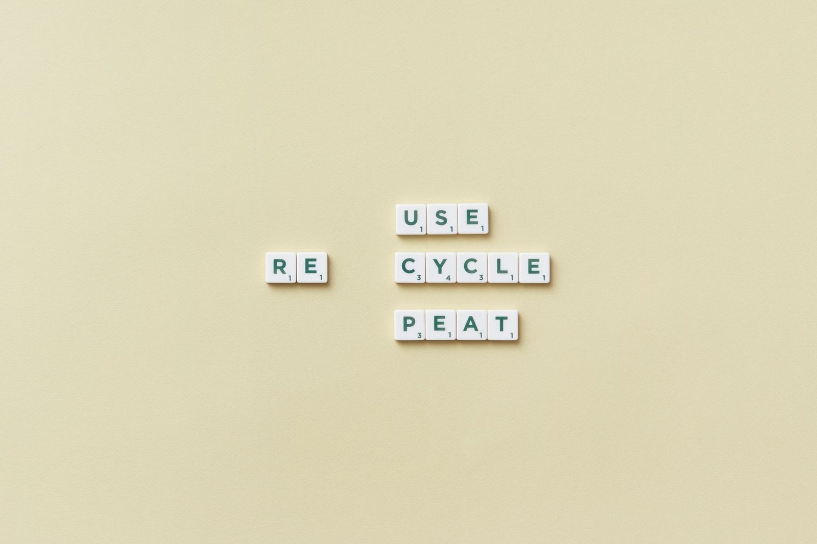 Letter tiles spelling 'reuse recycle repeat' on a simple background, promoting sustainability.