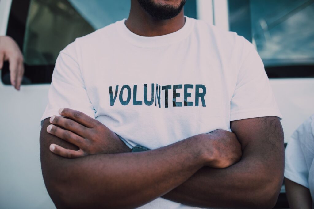 A close-up of a person wearing a volunteer shirt with arms crossed, promoting community service.