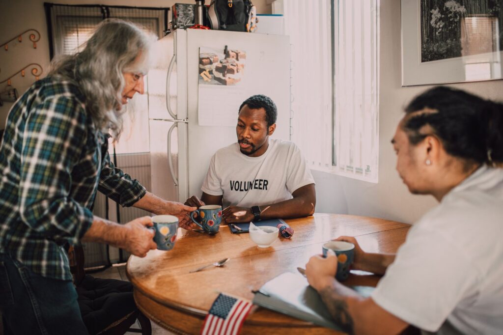 Three volunteers sharing coffee and ideas in a cozy kitchen setting, promoting community engagement.