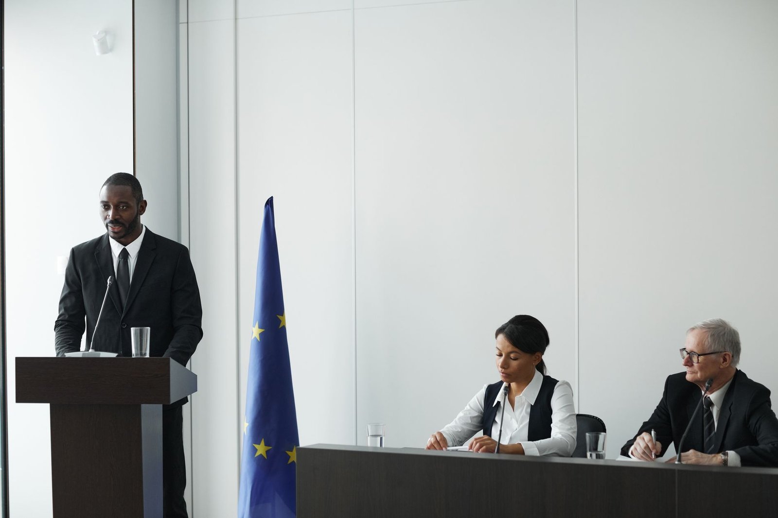 Professional business conference with EU flag, diverse speakers in suits discussing diplomacy.