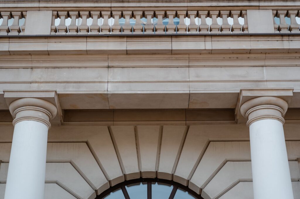 Low angle view of a neoclassical building facade featuring pillars and a balcony in daylight.
