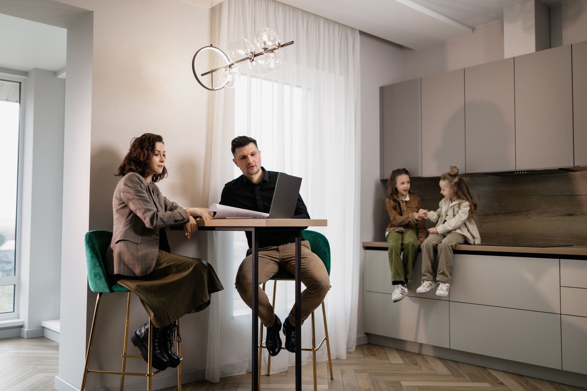 A modern family sitting together at home, using a laptop in a stylish kitchen setting.
