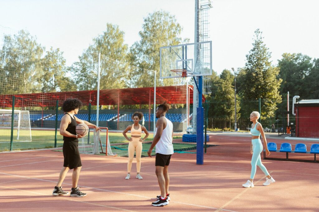 A diverse group of young adults playing basketball on an outdoor court during the day.