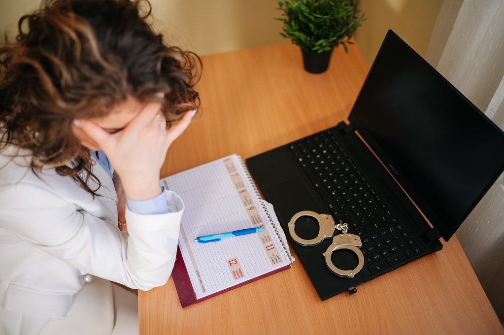 Worried online entrepreneur sitting at her desk with laptop and hand cuffs