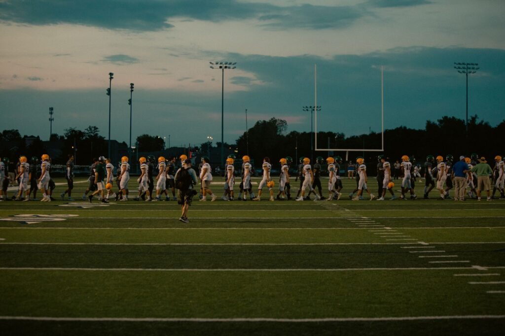 Players walking off football field at dusk after the game ends.