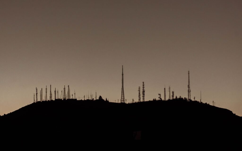 Silhouette of numerous communication towers on a hill during sunset.