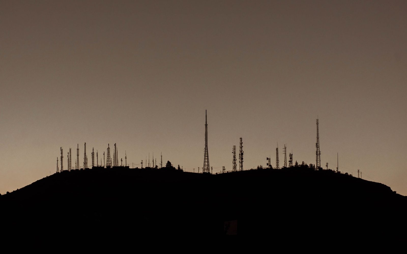 Silhouette of numerous communication towers on a hill during sunset.