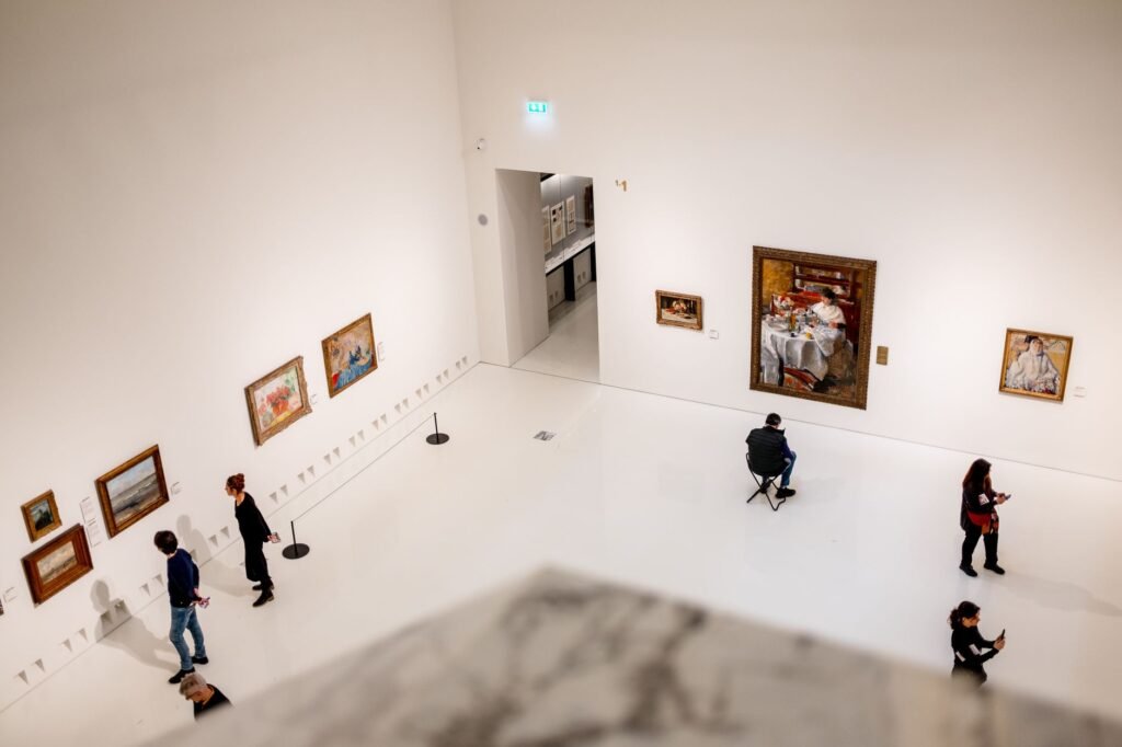Visitors exploring an art gallery with various paintings on display from a high angle view.