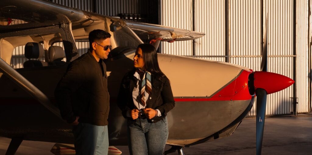 A couple standing beside a small aircraft inside a hangar, bathed in warm sunset light.