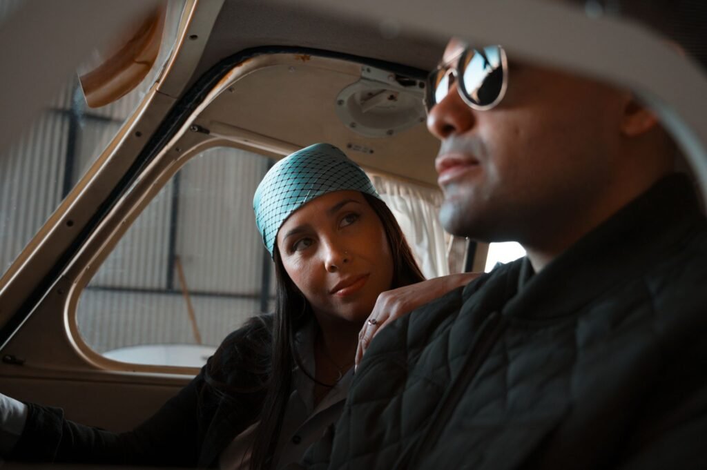 A stylish couple in an airplane hangar sharing a quiet moment inside a light aircraft.