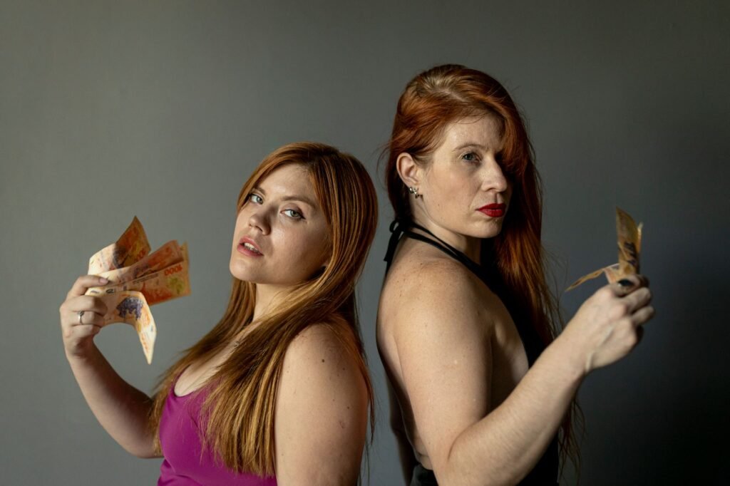 Portrait of two women displaying Argentine pesos. Shot indoors with a confident look.