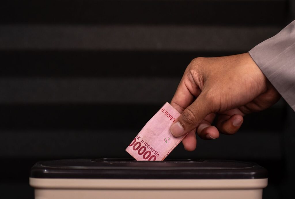 Close-up of a hand placing a 100,000 Indonesian Rupiah note into a donation box, highlighting charity and giving.