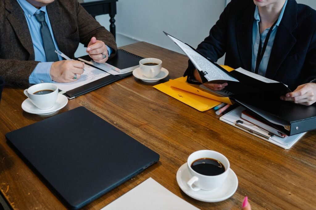 Crop unrecognizable coworkers in formal clothes sitting at table with documents and cups of coffee while working together