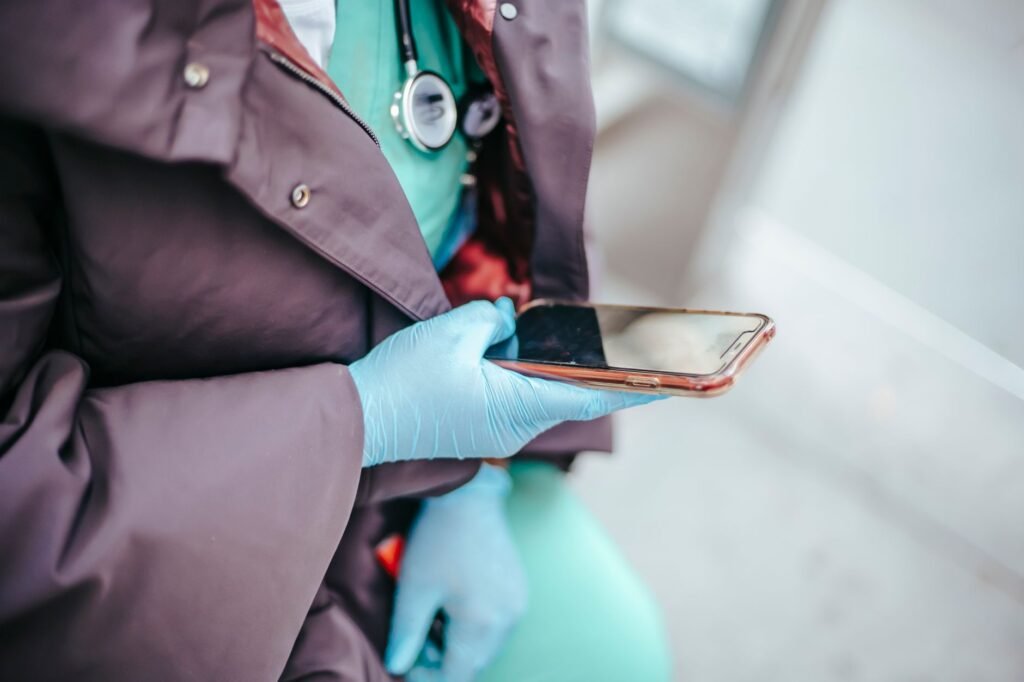 From above of crop unrecognizable female physician in outerwear touching black screen on mobile phone in daylight