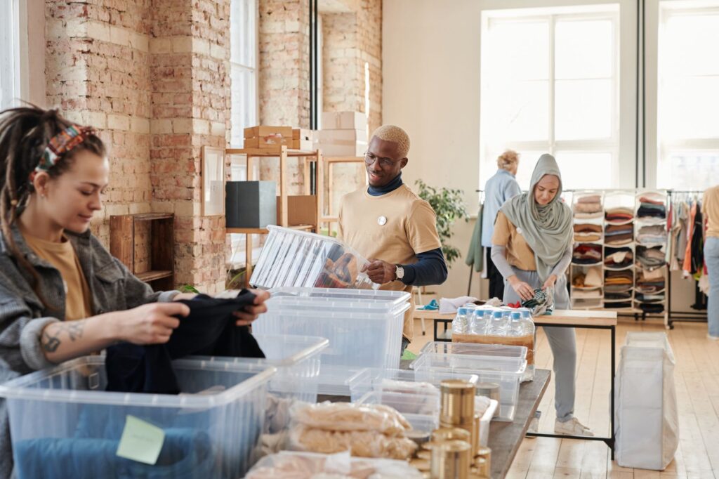 Group of diverse volunteers organizing donated clothing and supplies in a bright, airy warehouse.