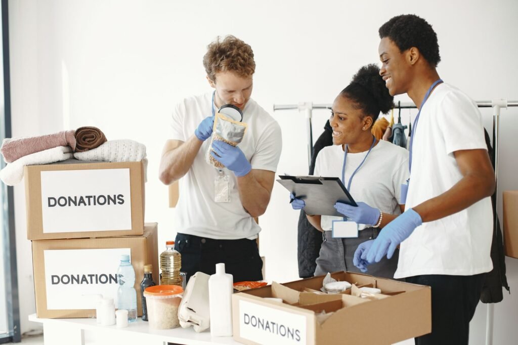 Three diverse volunteers sorting donation boxes filled with clothing and supplies indoors.