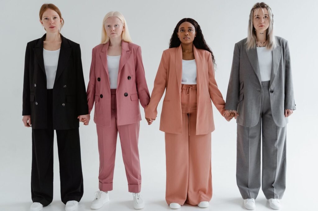 Four diverse women in stylish suits holding hands against a white background.