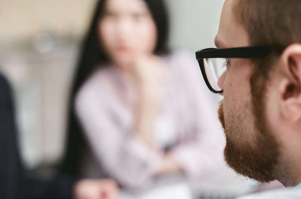 Close-up of a man in glasses with blurred colleagues in a business setting.