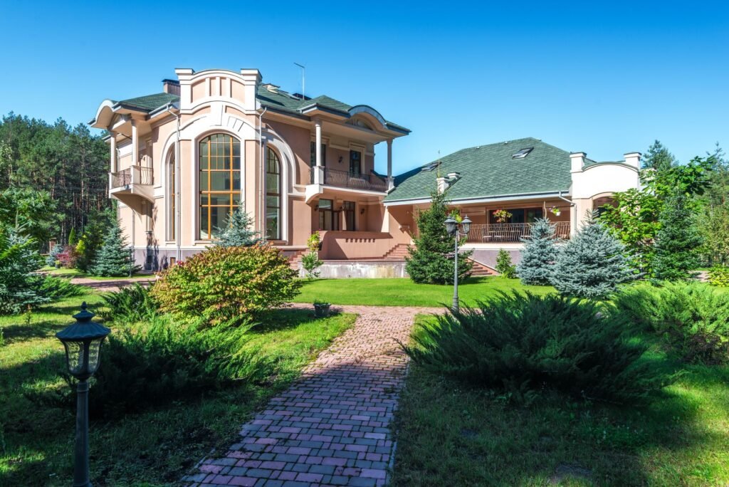 Beautiful mansion in sunny weather, surrounded by lush greenery and a clear blue sky.