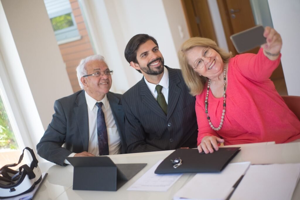Elderly couple taking a selfie with a realtor in an office setting, conveying a joyful real estate moment.