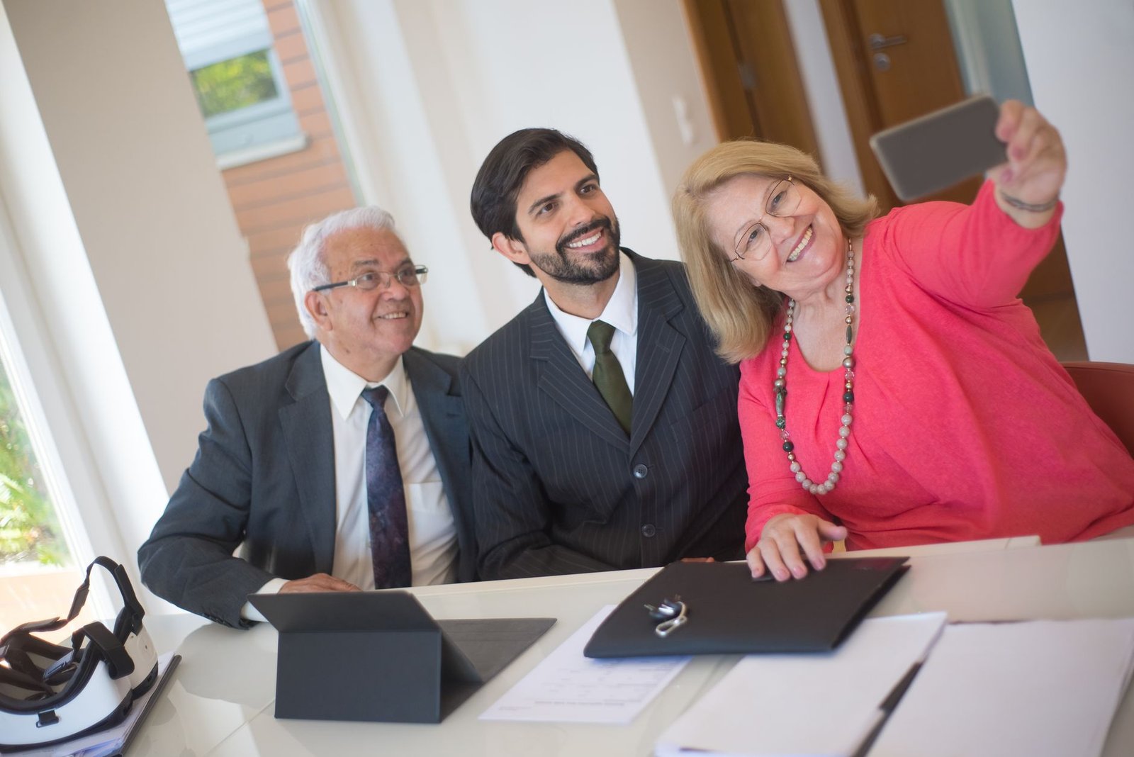 Elderly couple taking a selfie with a realtor in an office setting, conveying a joyful real estate moment.