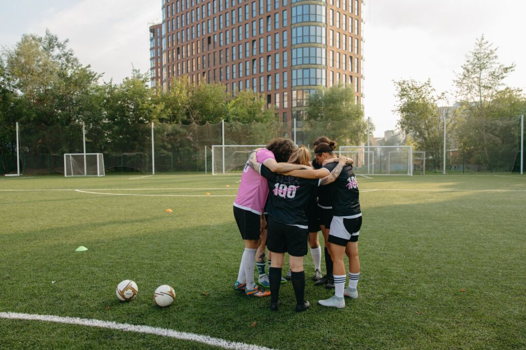Female soccer players in a huddle on a grass soccer field, preparing for a match.