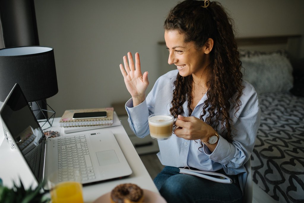 Woman enjoying virtual meeting with coffee in a cozy modern workspace at home during the day