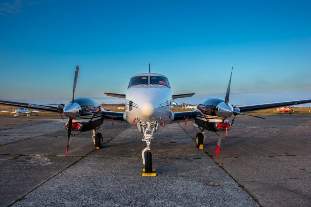 A front view of a twin-engine aircraft on tarmac under clear blue skies.