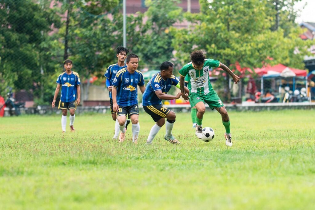 Competitive soccer game featuring local teams in action on a grassy field with players in colorful uniforms.