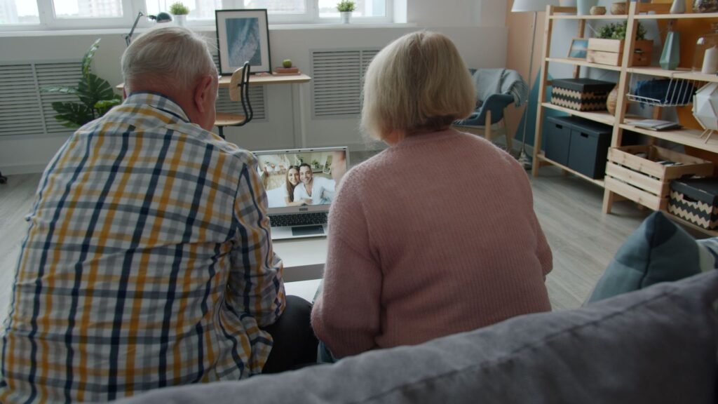 Elderly couple video chatting with family on laptop in cozy living room setting.