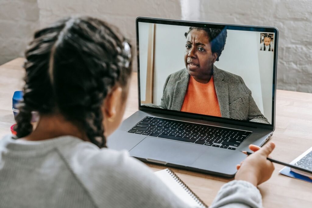 Back view of smart ethnic girl talking with tutor about test online on laptop