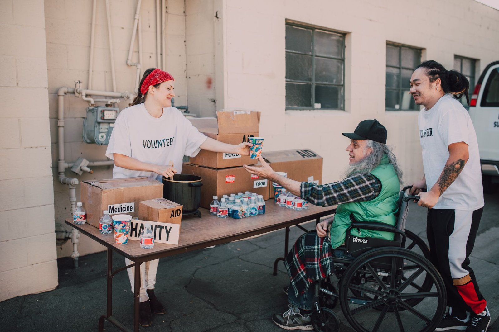 Volunteers handing out aid packages and drinks to a person in a wheelchair. Acts of kindness and charity.