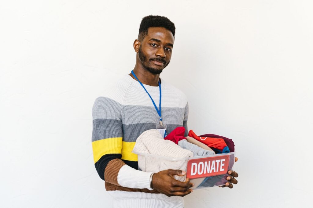 Smiling volunteer holding a donation box filled with clothing against a white background.