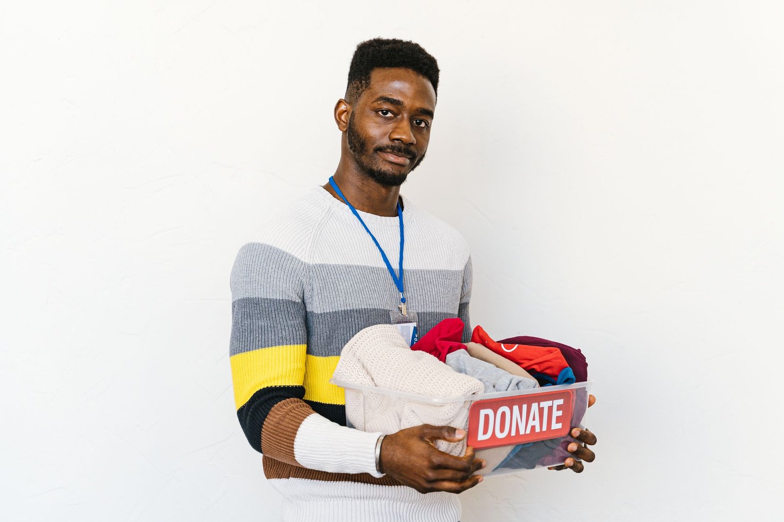 Smiling volunteer holding a donation box filled with clothing against a white background.