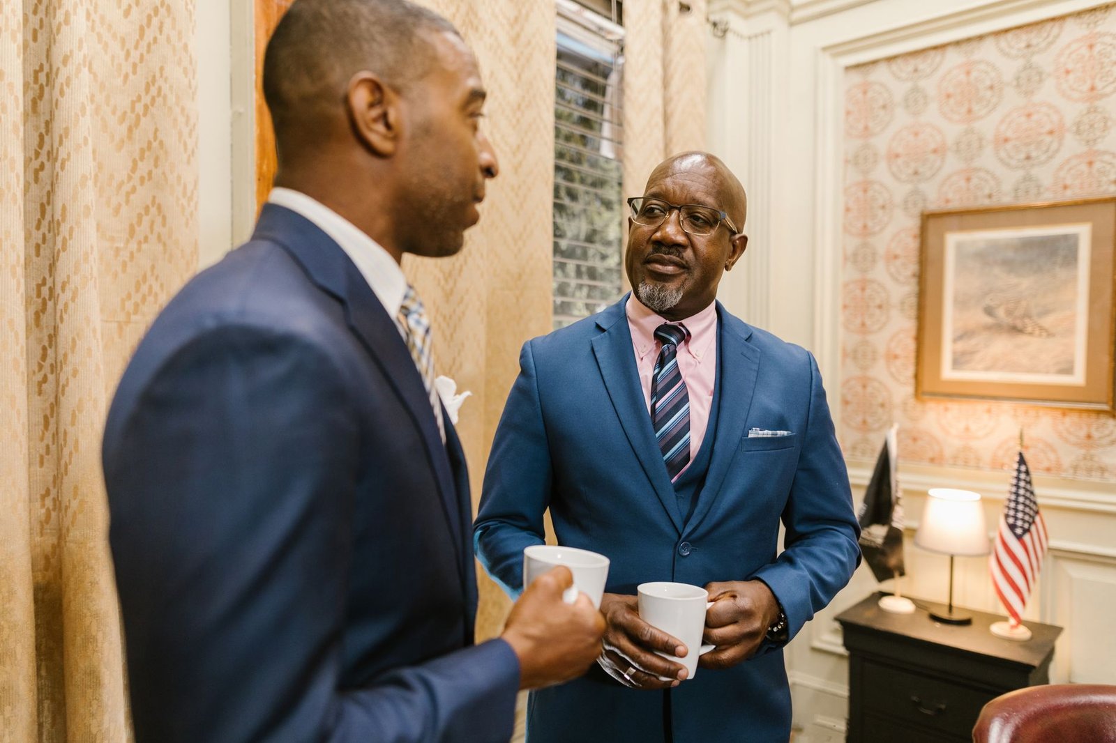 Two businessmen in suits having a coffee break and discussing business indoors.