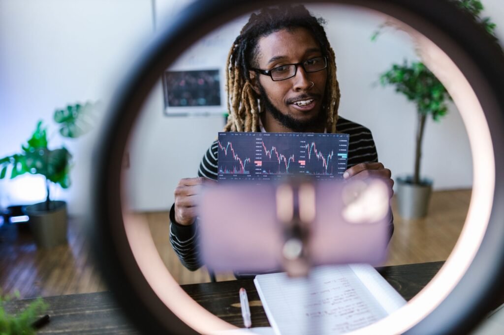 A vlogger reviews cryptocurrency stock charts in a modern setting with a ring light.