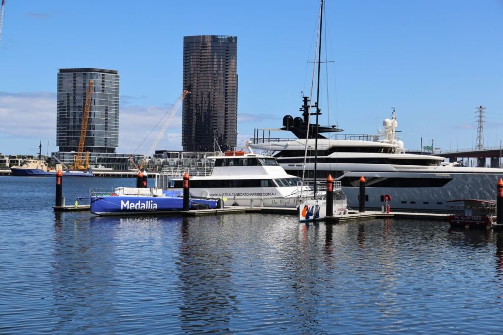 Luxury yachts docked at a marina with skyscrapers in the background under a clear sky.